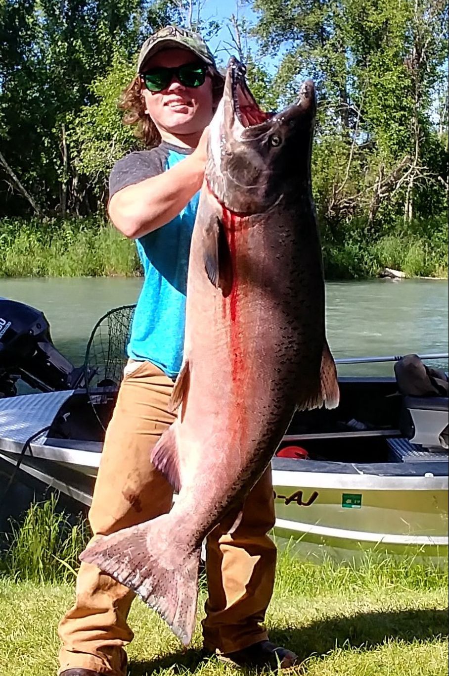 Happy fishing charter guest holds up massive trophy king salmon catch.