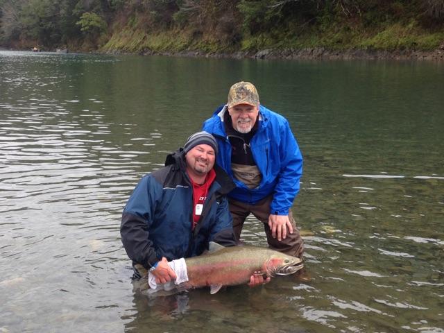 Fishing guide and guest smile with a nice catch of a large steelhead, in the river.
