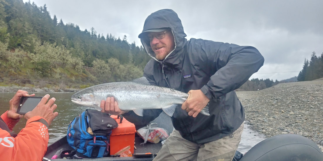 Guest holds up steelhead catch during a fishing charter on the Rogue River.